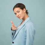 A young woman in a blue suit exhibits confidence with a relaxed pose against a blue background.